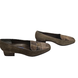 Peut inclure: Une paire de mocassins à talon en daim marron avec un motif à carreaux sur l'orteil. Les mocassins ont un talon bas et une pointe pointue.