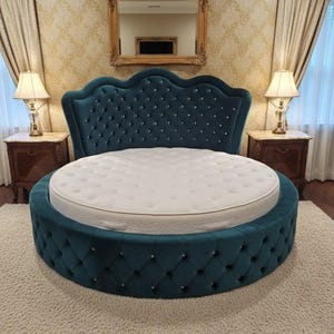 May include: A teal, round bed with a tufted headboard and base. The headboard has a scalloped top and is adorned with crystal-like buttons. A white mattress sits atop the bed frame. The bed is on a cream-colored rug.