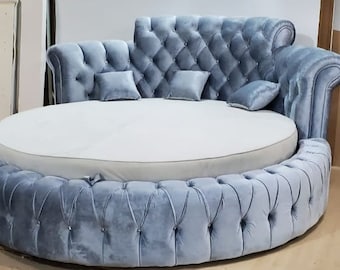 Könnte beinhalten: Ein rundes, gepolstertes Bett mit einem hellblauen Samtbezug. Das Bett hat eine weiße Matratze und ein Kopfteil mit gepolsterten Kissen.