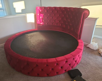 May include: A round, red velvet bed with a tufted headboard. The bed is upholstered in a deep red velvet fabric and has a tufted design on the headboard and the base.