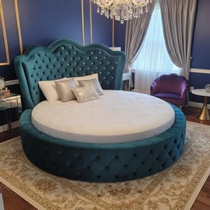 May include: A teal, round bed with a tufted headboard and base. The headboard is adorned with diamond-shaped button tufting. The bed is placed on a patterned rug in a bedroom with blue walls, gold trim, and a chandelier.