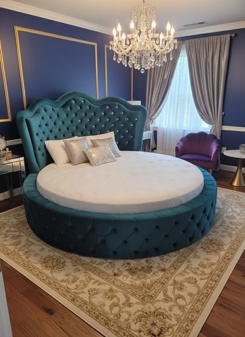 May include: A teal, round bed with a tufted headboard and base. The headboard is adorned with diamond-shaped button tufting. The bed is placed on a patterned rug in a bedroom with blue walls, gold trim, and a chandelier.