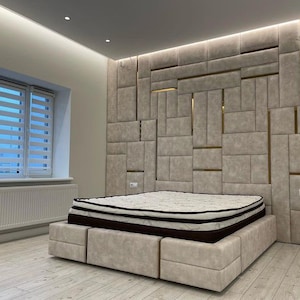 May include: A modern bedroom with a large bed featuring a tufted headboard with gold accents. The headboard is made of a light gray fabric and is divided into squares. The bed is sitting on a light wood floor.
