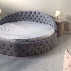 May include: A round gray tufted bed with a white mattress and two bedside tables with lamps.