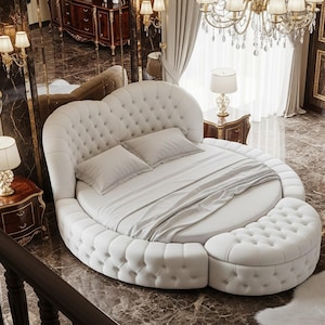 May include: A luxurious, round bed with a tufted headboard and base, upholstered in white fabric. The bed includes a matching ottoman and is adorned with pillows and bedding. The room features a chandelier, lamps, and a mirrored wall, creating an elegant ambiance.
