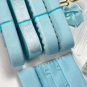 May include: Assortment of light blue elastic bra straps, including plain, scalloped, and satin styles. Also included is a light blue bra hook and eye closure.