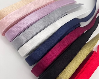 May include: A stack of ten different colored elastic bands. The colors are gold, red, black, burgundy, navy blue, white, silver, lavender, pink, and beige.