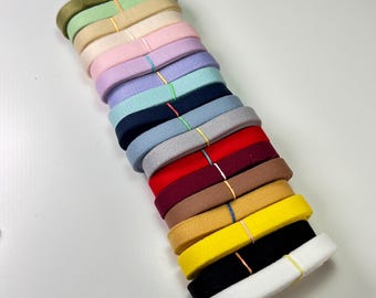 May include: A stack of colorful felt ribbons in various shades, including green, pink, purple, blue, red, brown, yellow, black, and white. Each ribbon is secured with a thin rubber band. The ribbons are arranged diagonally against a white background.