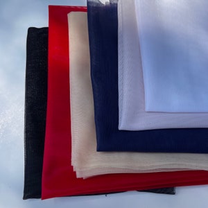 Op de afbeelding: Een stapel van vijf verschillende gekleurde tule stoffen. De stoffen zijn zwart, rood, beige, marineblauw en wit.