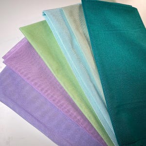 Könnte beinhalten: Ein Satz von sechs Stoffproben in verschiedenen Grüntönen, Blau- und Violetttönen. Die Proben sind fächerförmig angeordnet, wobei die dunkelste Farbe oben und die hellste Farbe unten ist.