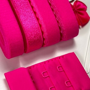 Könnte beinhalten: Ein Set aus rosa BH-Trägern und einem rosa BH-Verlängerer mit drei Haken. Die Träger sind aus verschiedenen Materialien, darunter Elastik und Spitze.