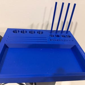 May include: A vibrant blue organizer tray with multiple compartments and vertical slots. The tray has a rectangular shape with a recessed area and several holes for holding items. The word "PARAFOOL" is printed on the side.