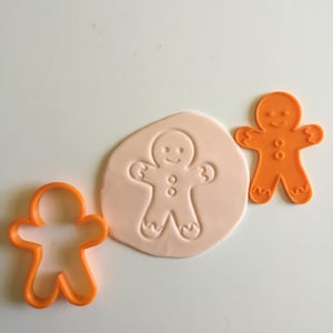May include: Two orange plastic gingerbread man cookie cutters. One cutter is imprinted into a piece of white fondant.