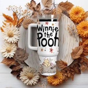 Puede incluir: Taza de viaje blanca con el texto "Winnie the Pooh" y detalles florales. La taza presenta una ilustraci&oacute;n de Winnie the Pooh y Piglet. La taza est&aacute; rodeada por una corona de follaje y flores de oto&ntilde;o.