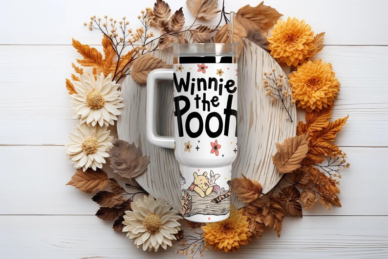 Puede incluir: Taza de viaje blanca con el texto "Winnie the Pooh" y detalles florales. La taza presenta una ilustraci&oacute;n de Winnie the Pooh y Piglet. La taza est&aacute; rodeada por una corona de follaje y flores de oto&ntilde;o.