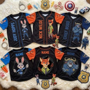 Op de afbeelding: Zwarte honkbalshirts met oranje en blauwe accenten, met personages uit Zootopia. De shirts tonen namen als "Judy Hopps", "Nick Wilde" en "Chief Bogo". Extra shirts hebben het woord "Name" op de rug.