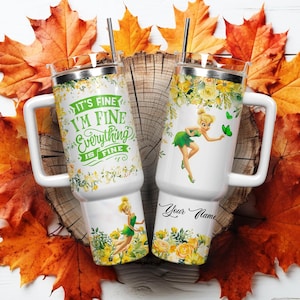 May include: Two white travel mugs with handles, featuring a floral design and the phrase "It's Fine, I'm Fine, Everything is Fine." One mug has a cartoon fairy. The mugs have a silver lid and a black straw. The background includes autumn leaves.