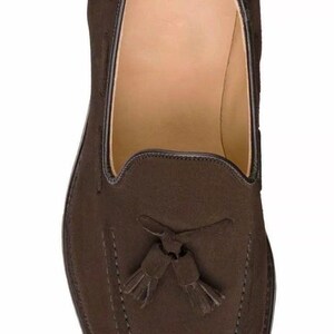 May include: Brown suede tassel loafers with a stitched design.