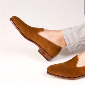 Men’s handmade brown suede slip-on loafers with leather sole, styled with light grey trousers