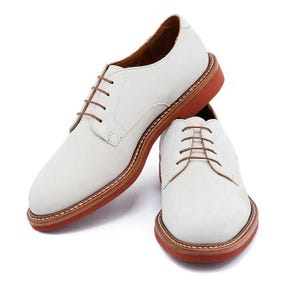 May include: A pair of white leather dress shoes with brown laces and a red sole. The shoes have a classic Oxford design. The shoes are displayed on a white background. The shoes are a UK size 9.