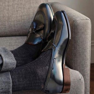 Black leather men's loafers with polished finish, classic slip-on design, elegant dress shoes styled with dark trousers and socks on a modern armchair