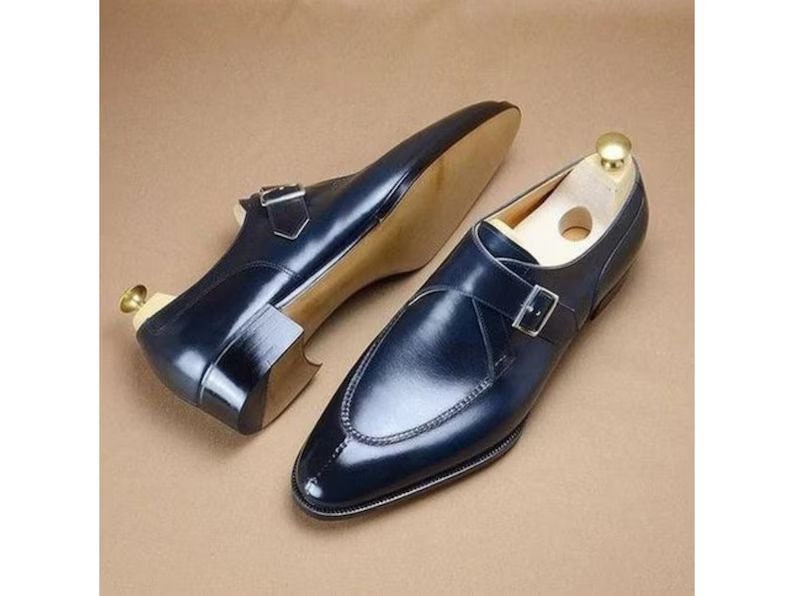 May include: A pair of dark blue leather dress shoes with a single buckle strap. The shoes have a pointed toe and a polished finish.