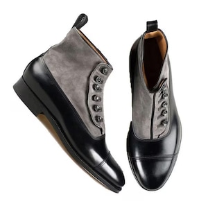 Puede incluir: Un par de botas de cuero negro con paneles de ante gris y cierres de botón. Las botas tienen una punta puntiaguda y un tacón bajo.