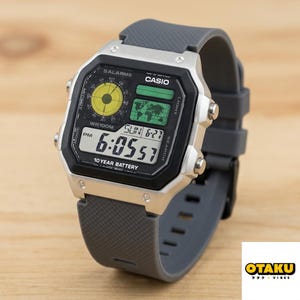 May include: A Casio digital watch with a gray strap and silver accents. The black watch face displays the time, date, and world map. The watch has the text "CASIO" and "10 YEAR BATTERY".
