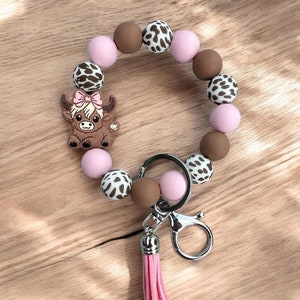 May include: A pink and brown silicone beaded keyring with a cow charm and a pink tassel.