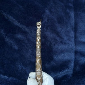 Puede incluir: Un abridor de botellas decorativo en forma de mano de plata y oro con un patrón geométrico. El abridor de botellas se sostiene con un guante blanco.