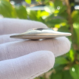 Könnte beinhalten: Ein silberner Ring mit einem einzigartigen, länglichen und leicht gekrümmten Design. Der Ring ist glatt und poliert, mit einem dezenten Glanz.