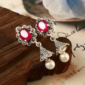 May include: A pair of silver earrings with red gemstone accents and pearl drops. The earrings feature a floral design with marcasite stones.