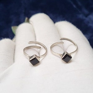 Puede incluir: Un par de anillos de dedo del pie de plata con piedras preciosas cuadradas negras.