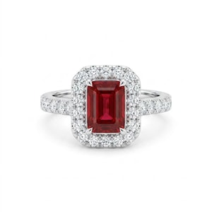 May include: A silver ring featuring a rectangular, deep red gemstone surrounded by a halo of smaller, clear gemstones. The ring's band is also adorned with small, clear gemstones, creating a sparkling effect. The ring is set against a white background.
