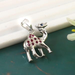 May include: A silver camel pendant with red and blue gemstones. The camel is standing on all four legs and has a hump on its back. The pendant is a great gift for anyone who loves animals or jewelry.