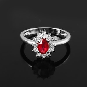 May include: A silver ring with a large oval ruby surrounded by smaller white diamonds.