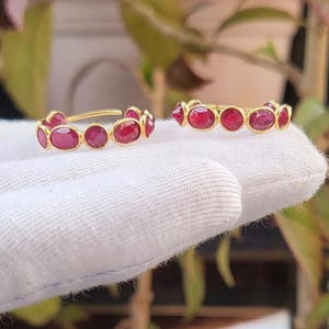 May include: A pair of gold hoop earrings with red gemstones. The earrings are made of a thin gold band with a row of oval-shaped red gemstones.
