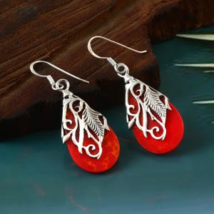 Puede incluir: Un par de pendientes de plata con gotas de coral rojo. Los pendientes presentan un delicado diseño de filigrana con hojas y espirales.