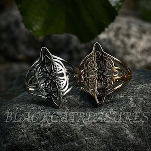 May include: Two Celtic knot rings, one silver and one gold, on a gray rock background.