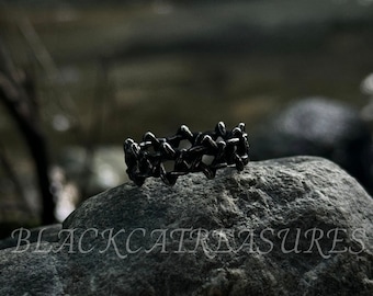 Könnte beinhalten: Ein dunkler, metallischer Ring mit einem komplizierten, geometrischen Design. Der Ring ist vor einem natürlichen Steinhintergrund platziert. Der Text "BLACKCAT TREASURES" ist unten im Bild zu sehen.
