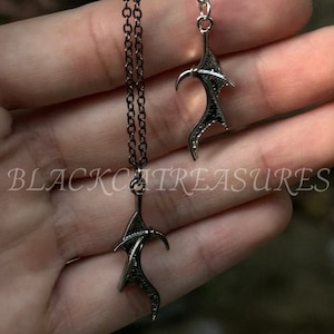 May include: Two silver necklaces with a wing-shaped pendant. The wings are detailed and have a gothic style.