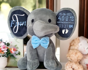 May include: Gray plush elephant toy with blue bow tie. The elephant's ears have a blue background with white text that reads "Finn" on one ear and "05-06-2023 4.0 KG 49 CM WEDNESDAY 03:27 AM" on the other ear.