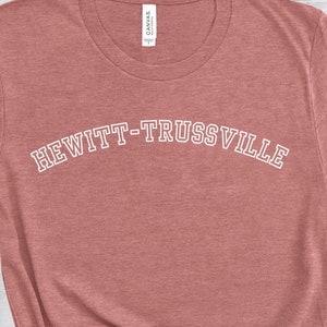 May include: A heather rose colored t-shirt with the text "HEWITT-TRUSSVILLE" in white outlined letters.