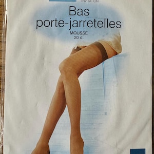 Peut inclure: Un paquet de bas beiges avec une étiquette qui indique "Bas porte-jarretelles Mousse 20 d. Invitation" et un logo pour "Phildar".