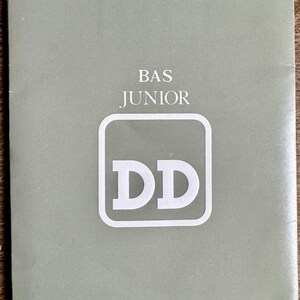 Peut inclure: Une brochure verte avec le texte "BAS JUNIOR" et un carré blanc avec les lettres "DD" à l'intérieur.