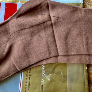 Peut inclure: Un gros plan sur un collant fin brun avec une couture dans le dos. Le collant est plié en deux et l'emballage est visible en arrière-plan. L'emballage est doré avec le texte "Avec Coton" et "Mallon" en blanc.