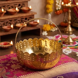 Puede incluir: Una cesta de metal en tono dorado pulido con un borde festoneado y un asa fina y arqueada. La superficie exterior está decorada con un patrón repetitivo de pequeñas hendiduras circulares en relieve y motivos florales alrededor.