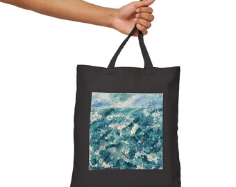 Puede incluir: Bolso tote negro con una pintura de un paisaje marino. La obra de arte representa un océano agitado en tonos azules y blancos, bajo un cielo azul claro. El bolso es sostenido por una mano.