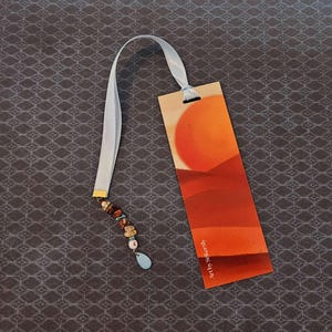 May include: A bookmark with a sunset scene and a beaded tassel. The bookmark is printed with the text "Art by SallieC."