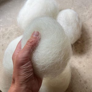 May include: Four balls of white fluffy yarn, one being held in a hand.